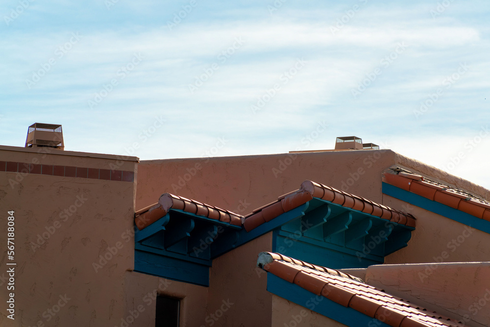 Multiple roof facades with ledges and visible chimney with blue and hazy white cloudy sky in late afternoon shade