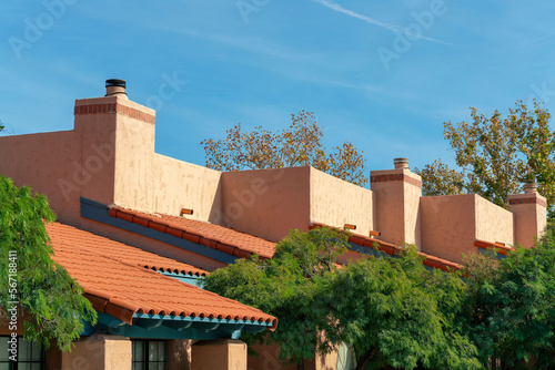Adobe style rooftops on apartment building or condo with chimneys and red roof tiles with front yard trees in desert