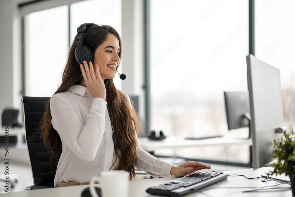Friendly female helpline operator in modern office. Young woman working as call center agent and holding headset with hand. Friendly female helpline operator in modern office. Young woman working as call center agent and holding headset with hand.