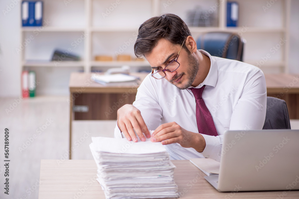 Young male employee and too much work at workplace Young male employee and too much work at workplace