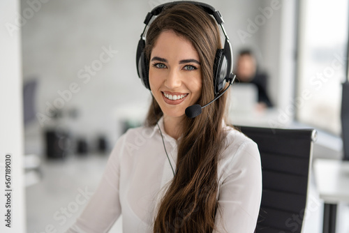 Close up portrait of service desk consultant woman talking using hands-free headphones with microphone. Smiling beautiful woman working as call center agent with headset in bright modern office.
