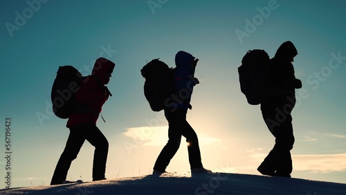 Silhouette of group of tourists, travelers, extending helping hand to each other, climbing snowy slope, mountains. Teamwork, business. Climbers man woman hand in hand. Teamwork business people partner