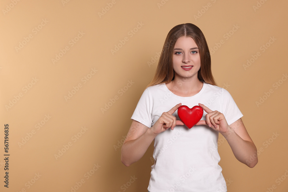 Young woman holding red heart on beige background, space for text. Volunteer concept Young woman holding red heart on beige background, space for text. Volunteer concept