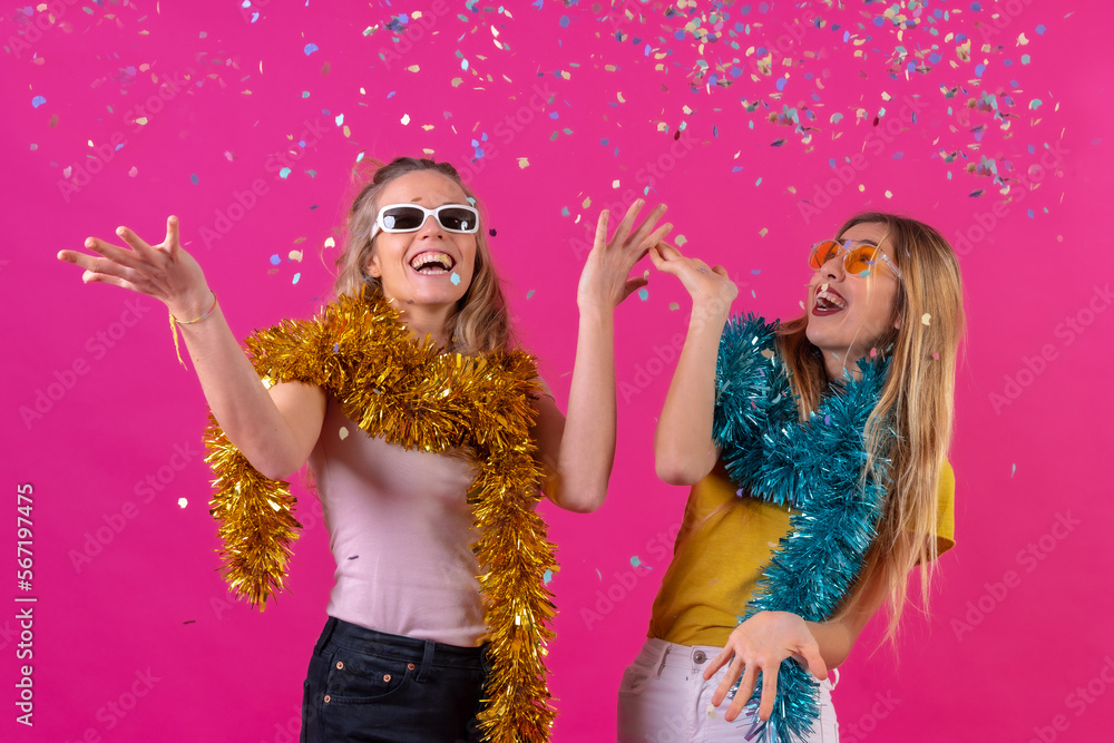 Two young blonde caucasian women partying, having fun throwing confetti, isolated on a pink background Two young blonde caucasian women partying, having fun throwing confetti, isolated on a pink background