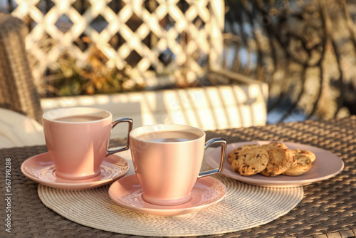 Cups with tasty cocoa and cookies on rattan table at balcony