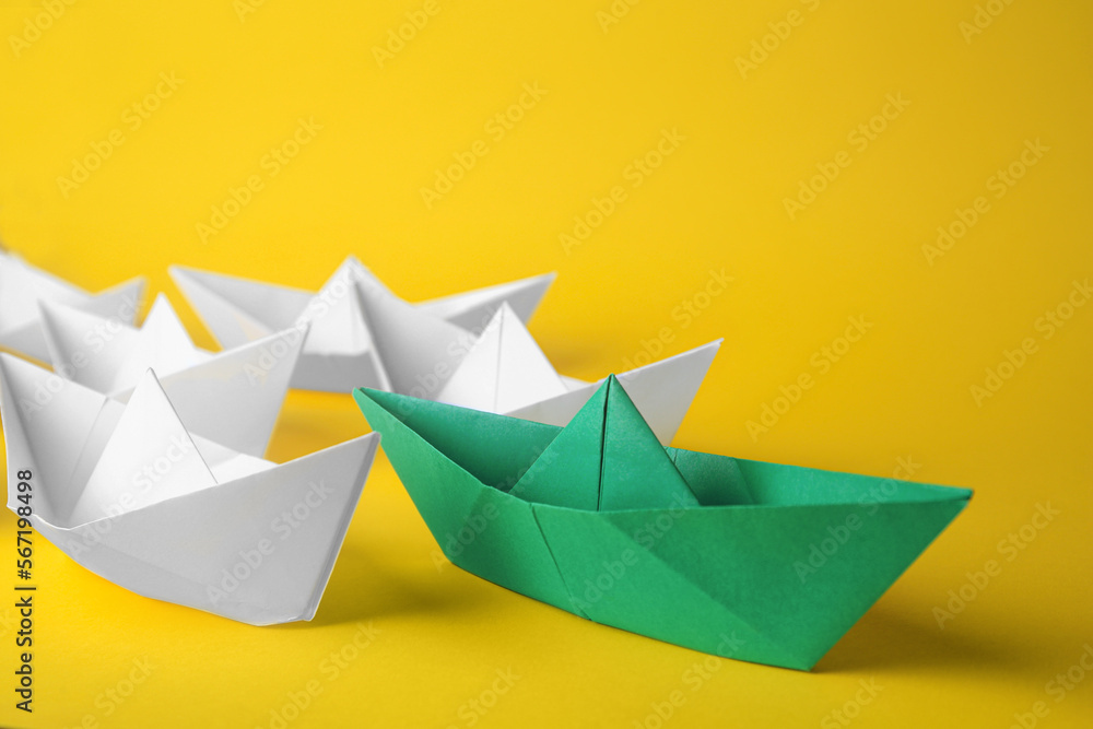 Group of paper boats following green one on yellow background. Leadership concept Group of paper boats following green one on yellow background. Leadership concept