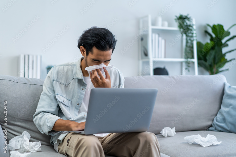 Asian handsome male having running nose while working in living room. Asian handsome male having running nose while working in living room.