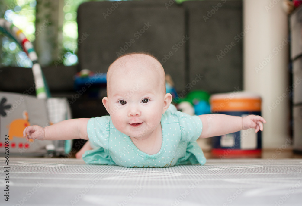 Infant baby girl on the floor during tummy time with her arms up like