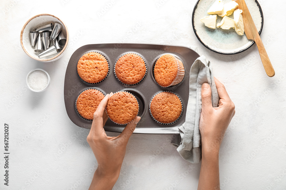 Female hands with tasty muffins, ingredients and piping tips on light