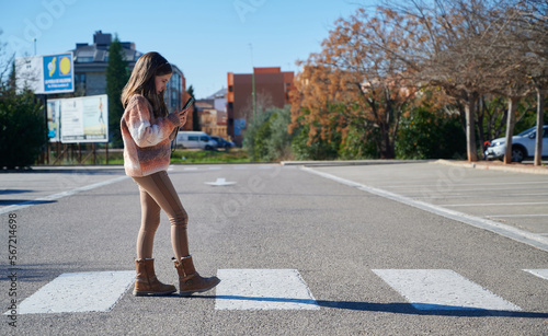 Child looking at the cellphone while crossing crosswalk photo