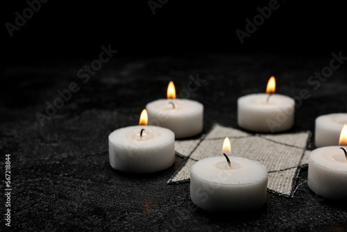Burning candles and Jewish badge on dark background with space for text. International Holocaust Remembrance Day