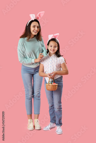 Beautiful woman and her little daughter in bunny ears with Easter eggs and rabbit on pink background