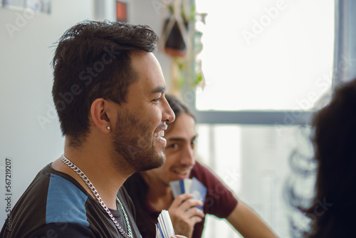 Young latin man with ear piercing smiling while playing cards with friends.