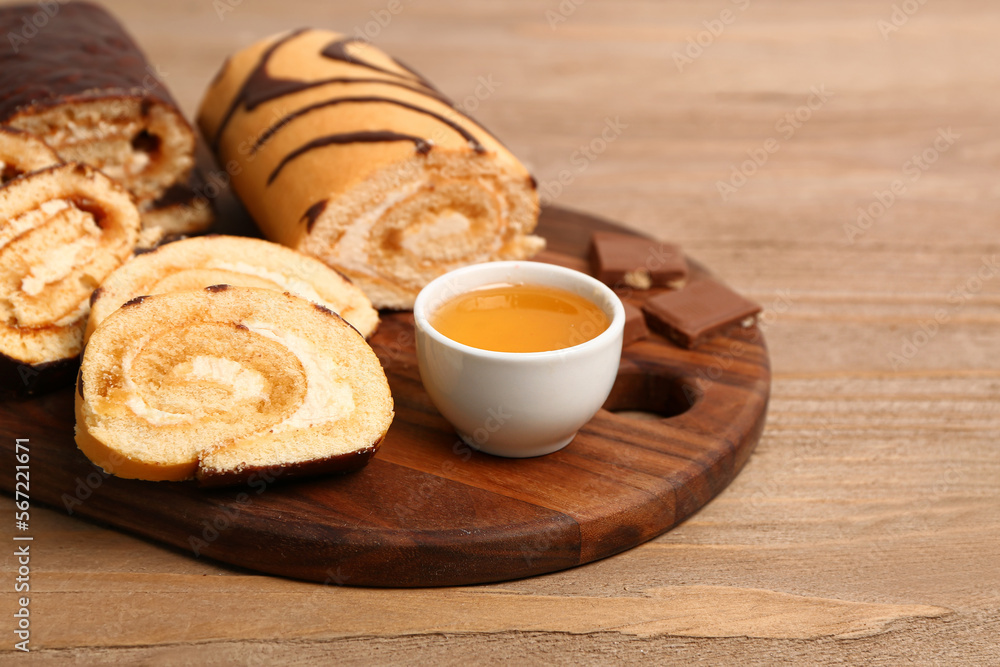 Board with pieces of delicious sponge cake roll, bowl of jam and chocolate on wooden table Board with pieces of delicious sponge cake roll, bowl of jam and chocolate on wooden table