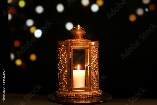 Lantern with burning candle on table against blurred lights. Islamic New Year celebration photo