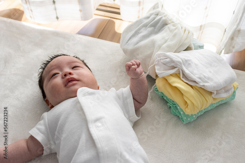 起きている赤ちゃんと畳んだ子供服（0歳2か月、日本人、男の子）