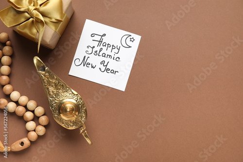 Card with text HAPPY ISLAMIC NEW YEAR, Aladdin lamp, gift and prayer beads on brown background photo