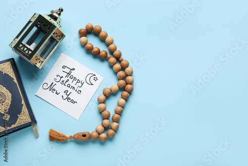 Card with text HAPPY ISLAMIC NEW YEAR, Koran, lantern and prayer beads on blue background photo