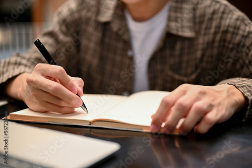Cropped shot of a male college student doing homework, writing or taking notes on his book © bongkarn
