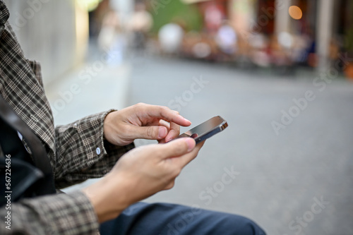 Side view of a man using his smartphone while relax sitting at the city square street.