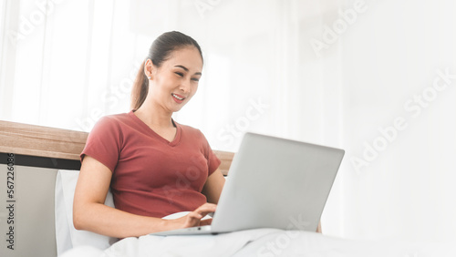 Young adult asian woman using laptop on bed for telemedicine mental health or shopping online
