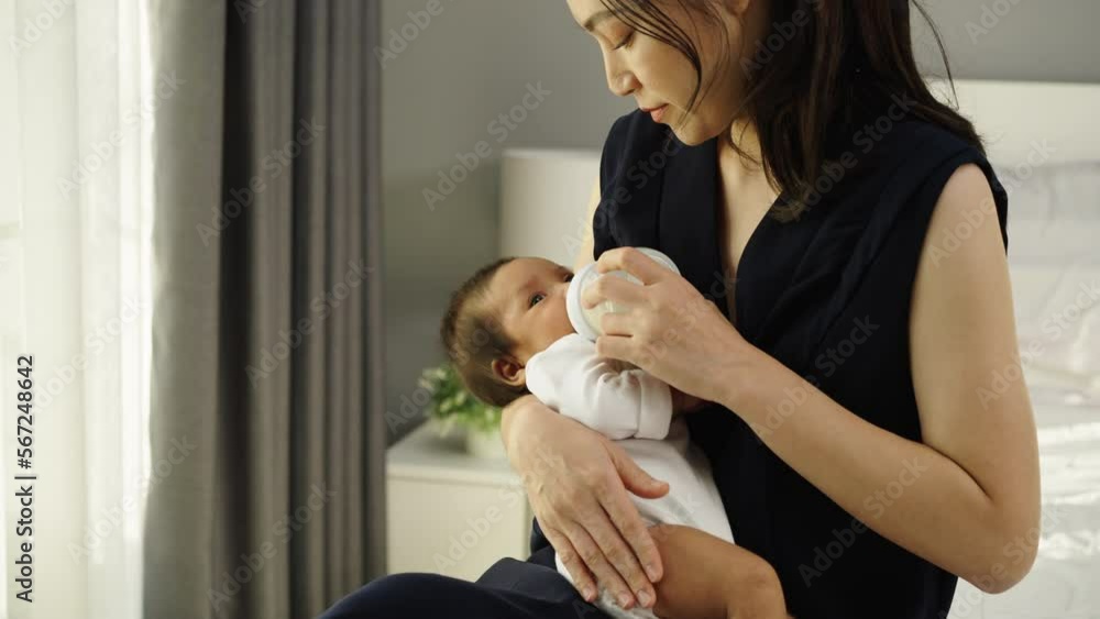 mother feeding milk bottle to her newborn baby on a bed mother feeding milk bottle to her newborn baby on a bed
