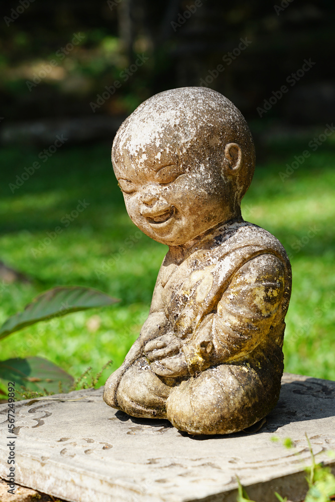 Child monk happy smiling laughing face doll Buddha, old stone art statue decoration in outdoor green scenery at Wat Pha Lat, Doi Suthep, Chiangmai temple, Thailand 