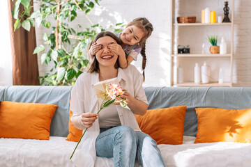 Daughter closed her mother's eye with her hands and gave a gift and flowers. mother's day