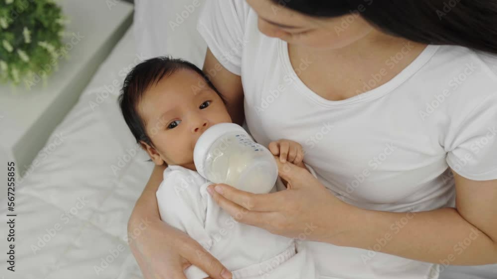 mother feeding milk bottle to her newborn baby on a bed mother feeding milk bottle to her newborn baby on a bed