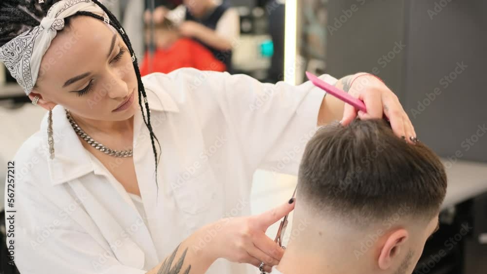 Stylish young girl hairdresser makes a haircut for a young man in a barbershop. She stands behind the client, finishing the job. Close-up Stylish young girl hairdresser makes a haircut for a young man in a barbershop. She stands behind the client, finishing the job. Close-up