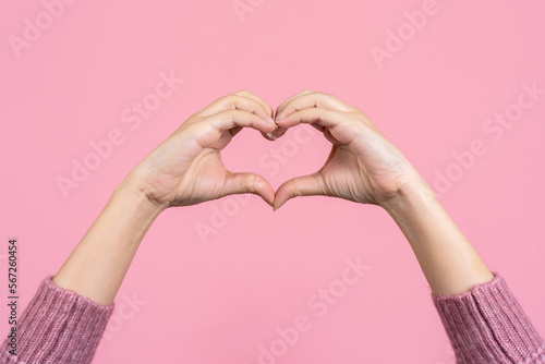 Female hands showing a heart shape isolated on a color light pink background. Sign of love  harmony  gratitude  charity. Feelings and emotions concept