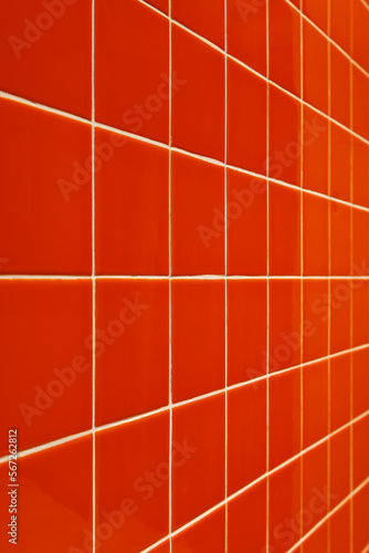 The wall is clad in modern orange glossy ceramic tiles with white grout. Angle view. Selective focus.