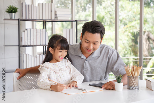 Children education and home school concept : Young asisn father pleased to see little daughters' study success. Excited smiling small child girl enjoying learning and writing with pleasant dad at home