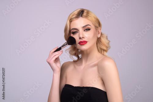 Studio portrait of a woman applying cosmetic tonal foundation on face using makeup brush. Beautiful girl doing contouring apply blush on cheeks isolated on studio background.
