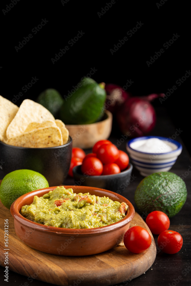 Overhead view of bowl with guacamole on dark table with spoon, nachos, tomatoes, avocados, limes and salt, selective focus, vertical, with copy space Overhead view of bowl with guacamole on dark table with spoon, nachos, tomatoes, avocados, limes and salt, selective focus, vertical, with copy space