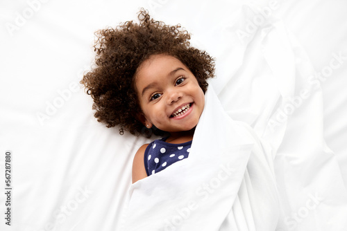 Happy little girl with afro hair lying on white bed