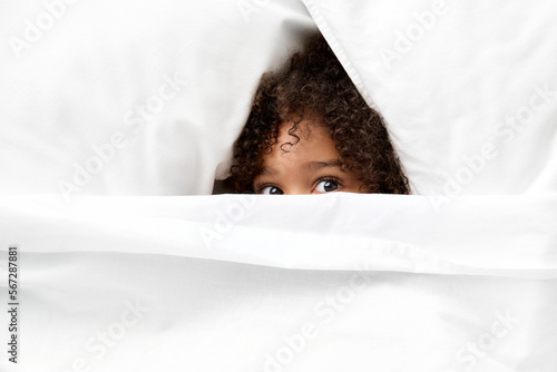 Little girl's eyes peeking from white sheet photo