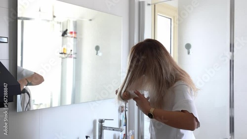 Woman styling hair with dryer styler care machine in bathroom. Young female using a modern rotative hair brush to style her hair. Thermal and ceramic coating rotating brush with attachments photo