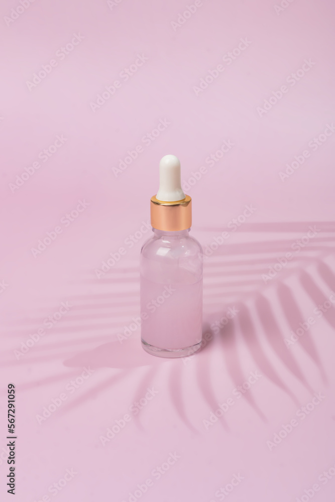Glass cosmetic bottle dropper with beuty oil or serum for skin care on pink background. Natural skin care concept. Hard shadows of palm tree Glass cosmetic bottle dropper with beuty oil or serum for skin care on pink background. Natural skin care concept. Hard shadows of palm tree