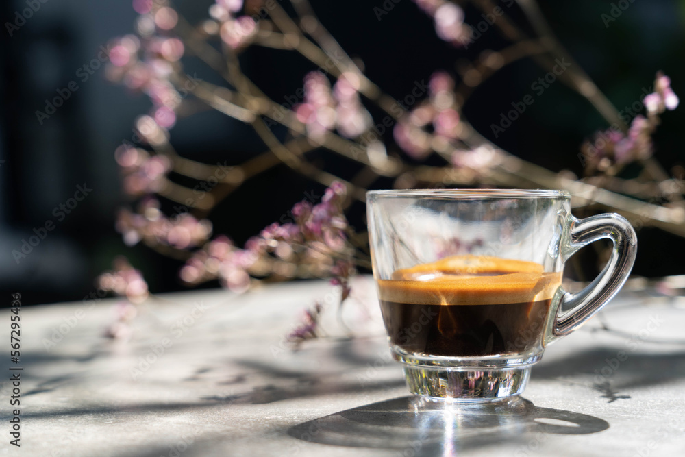 Espresso shot coffee in clear small cup with blur pink flower in background in the morning Espresso shot coffee in clear small cup with blur pink flower in background in the morning