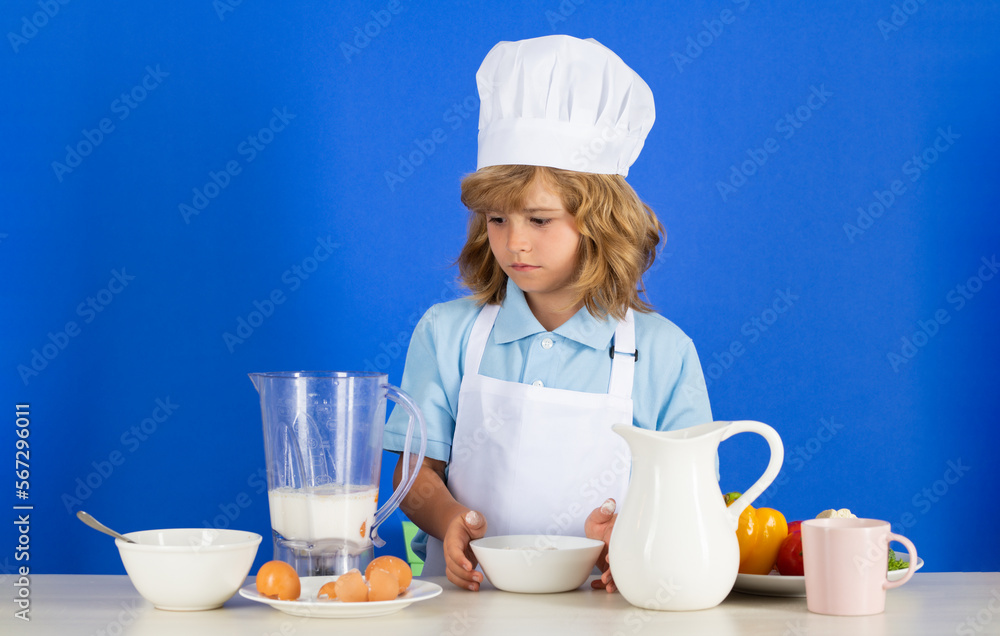 Kid boy in chef hat and apron cooking preparing meal. Little cook with vegetables at kitchen. Natural kids food. Kid boy in chef hat and apron cooking preparing meal. Little cook with vegetables at kitchen. Natural kids food.