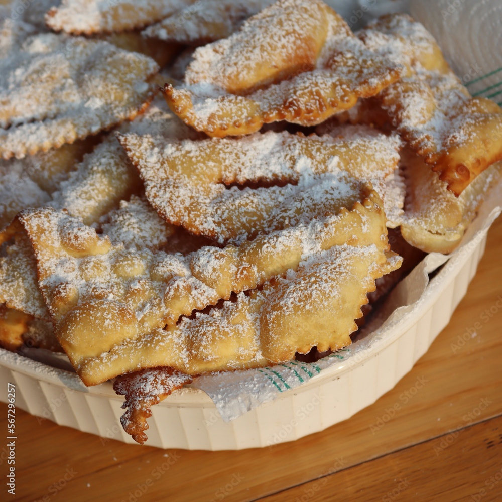 Italian Carnival pastry. Traditional carnival sweet crisp pastry deep-fried and sprinkled with powdered sugar. Chiacchere or crostoli, bugie, cenci  in a white plate on wooden table 