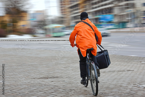 Man on bicycle delivering food in orange uniform, courier cycling with pizza bag, deliver food to customers. Worker with thermal backpack delivering pizza from restaurant.