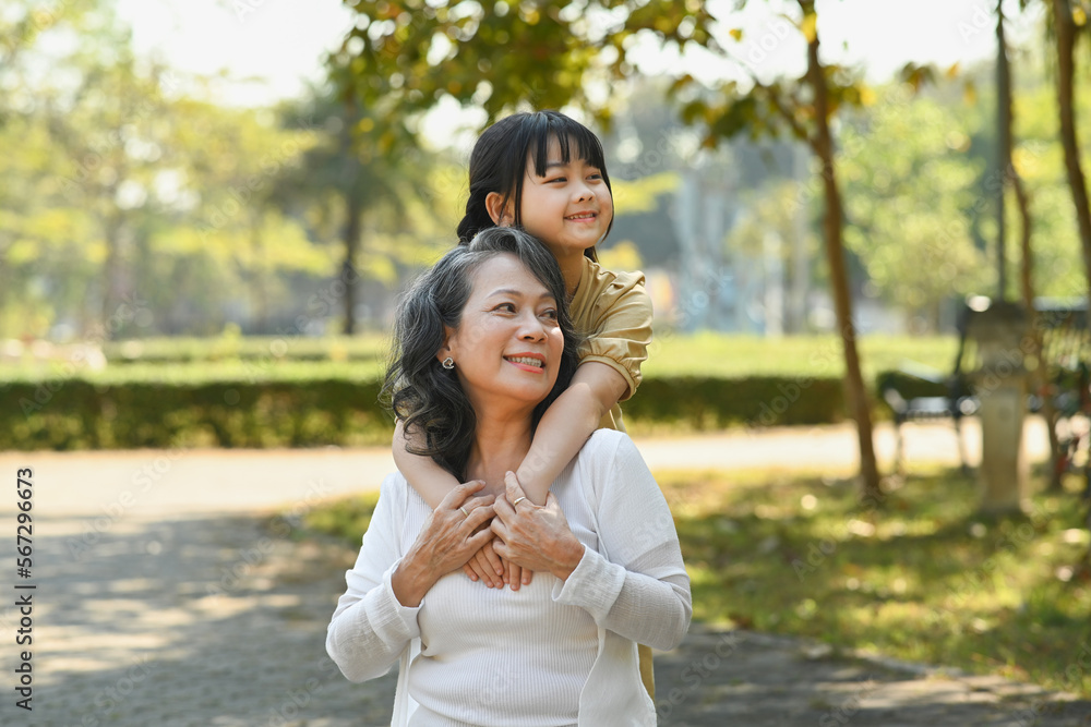 Naklejka premium Happy moments with grandmother and little granddaughter walking in the park surrounded by green trees at sunlight morning