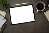Flat lay digital tablet with white empty display, stylus pen, coffee cup and notepad on black slate texture background