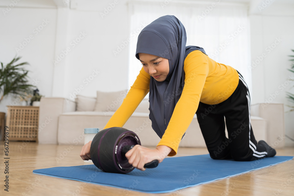 Happy Asian muslim woman in hijab workout on mat at home. Smiling muslim female exercising on floor in living room