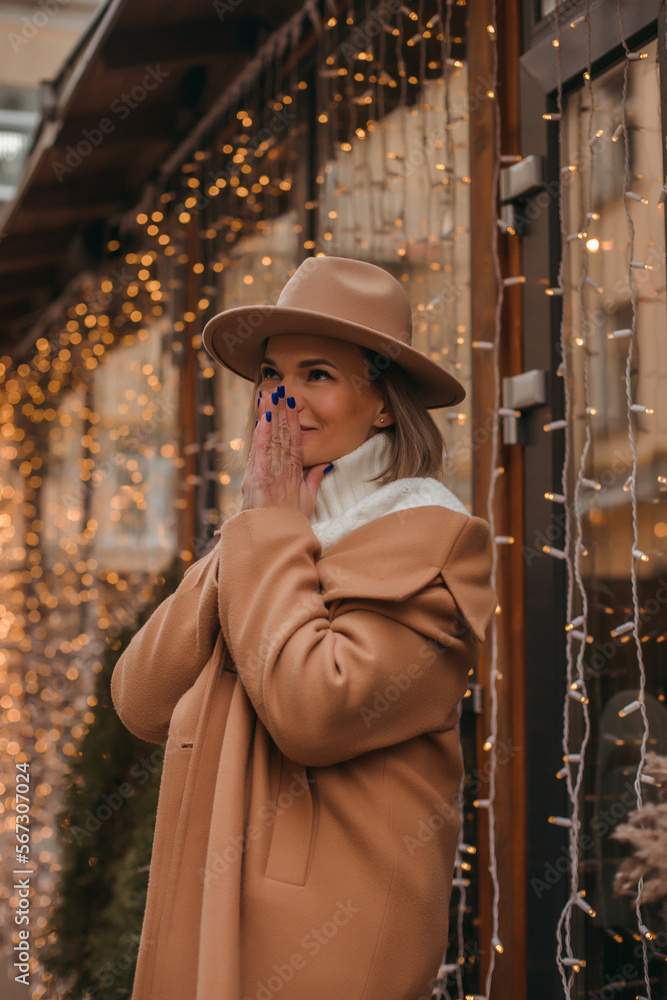 Outdoor fashion portrait of an elegant woman in a beige hat and coat posing in a european city.