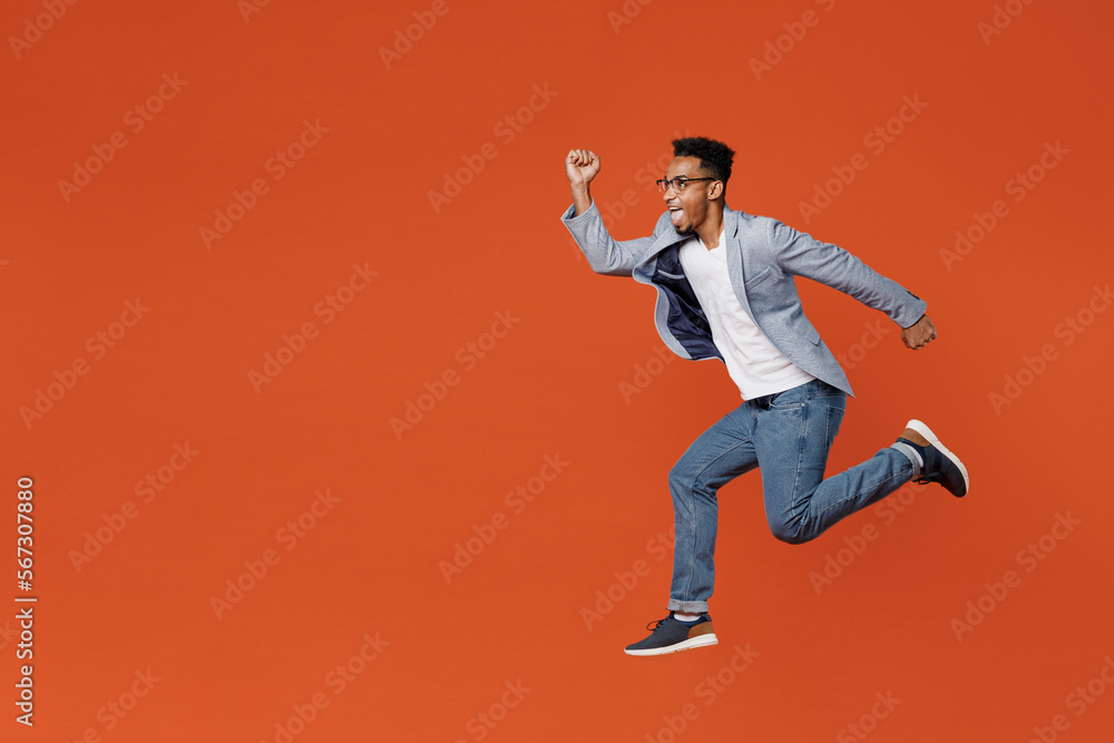 Full body side profile view young employee business man corporate lawyer wear classic formal grey suit shirt glasses work in office jump high run fast isolated on plain red orange background studio.