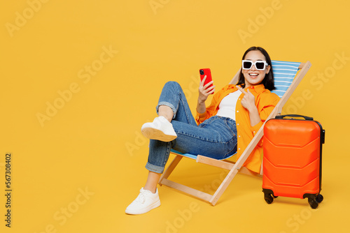 Young woman wear summer clothes sit in deckchair use show mobile cell phone isolated on plain yellow background. Tourist travel abroad in free spare time rest getaway. Air flight trip journey concept. #567308402