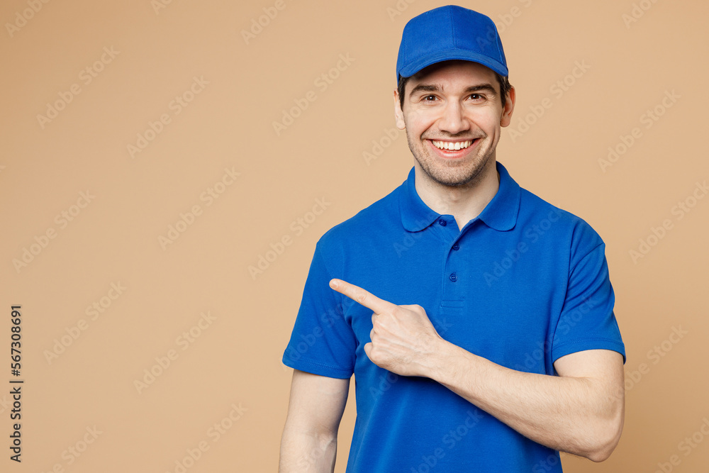 Happy delivery guy employee man wearing blue cap t-shirt uniform workwear work as dealer courier pointing index finger aside indicate on area isolated on plain light beige background. Service concept. - obrazy, fototapety, plakaty 